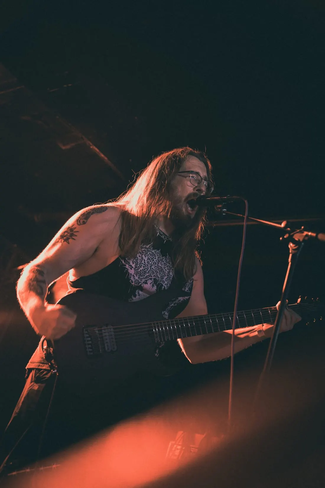 Guitarist and vocalist at the mic under warm light, July 2026