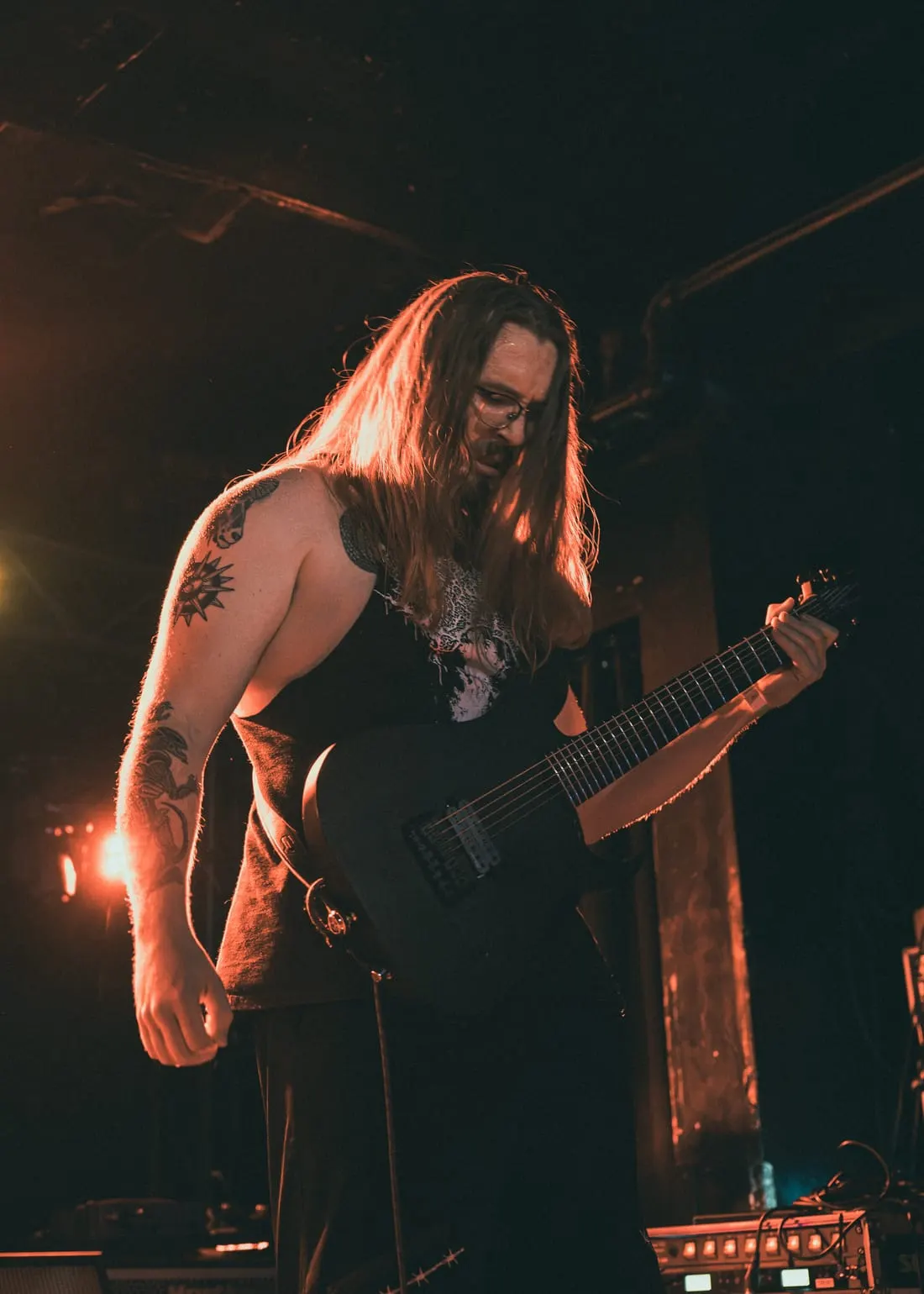Guitarist bent over the strings under amber light, July 2026